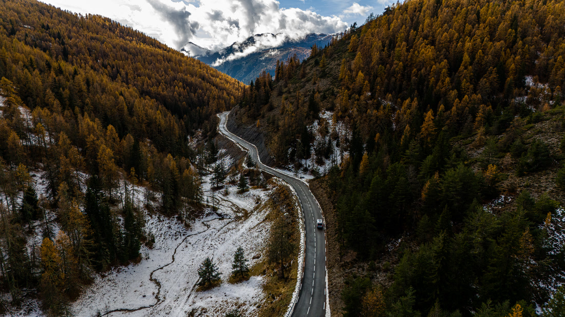 Carretera de montaña entre alerces otoñales y nieve, vista aérea